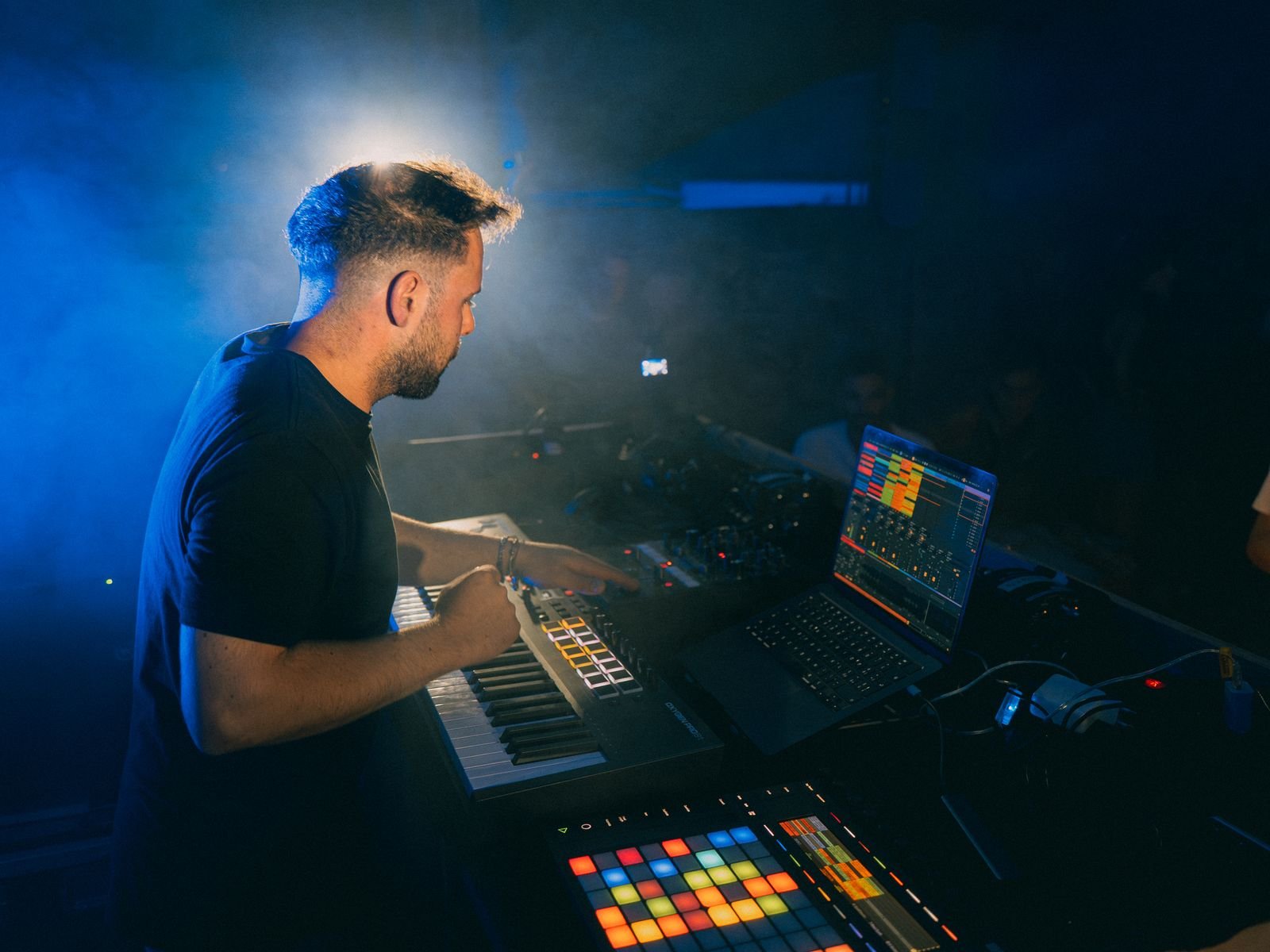 Alessio al suo set live, tra tastiera, pad e computer, in luce blu