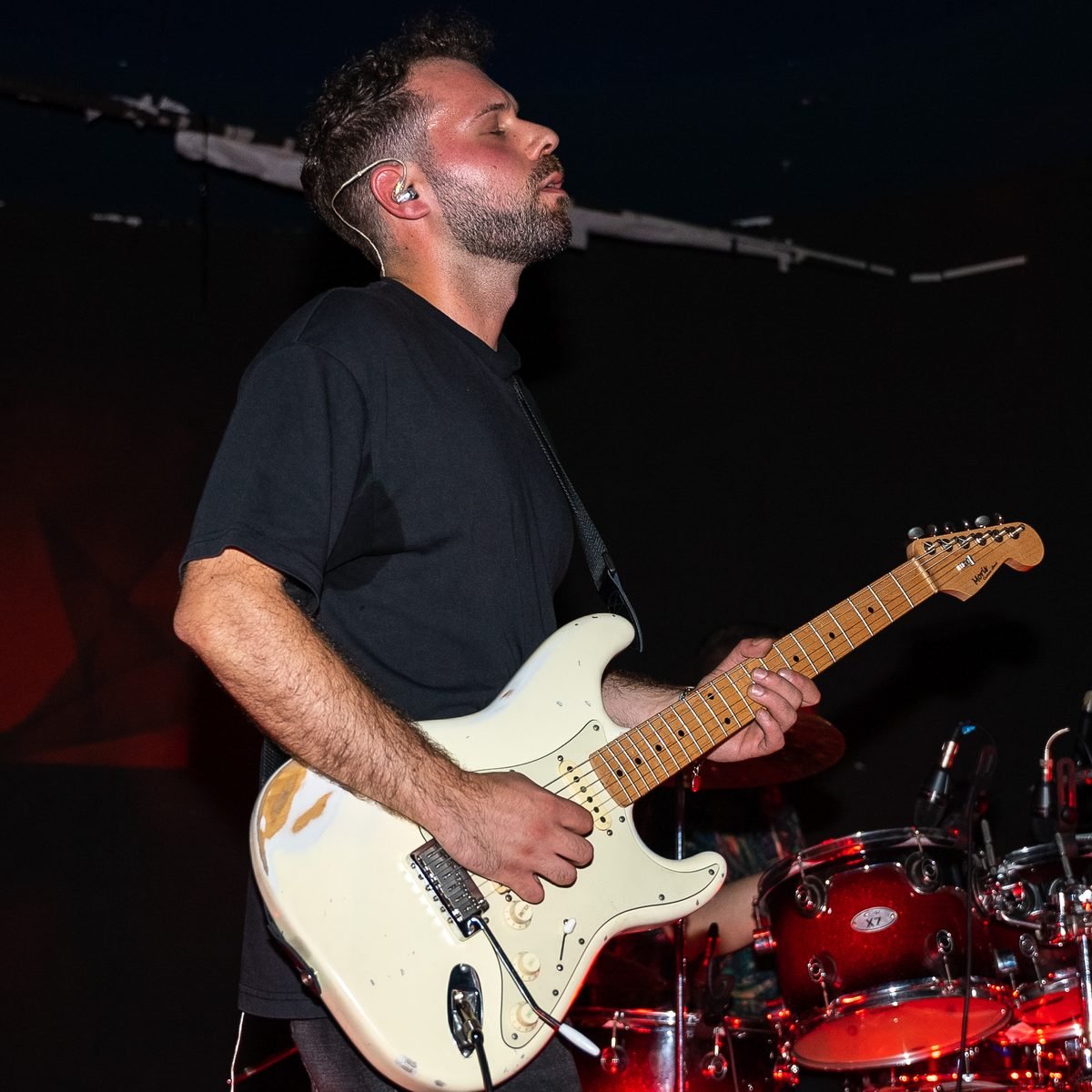Alessio dal vivo con la Stratocaster bianca, in controluce rosso, la batteria alle spalle